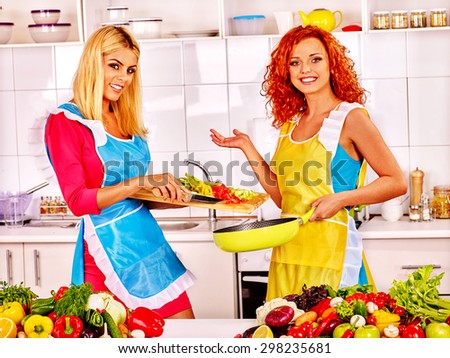 Happy couple women in aprons preparing food at kitchen.