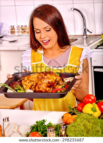 Happy young woman in yellow cooking chicken at home kitchen.