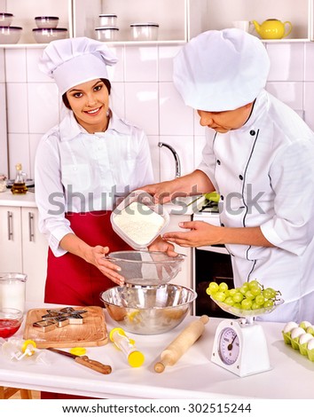 Happy smiling young woman and man in chef hat cooking dough .Grapes in foreground