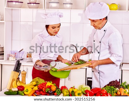 Happy man and young woman professional in chef hat cooking chicken together.
