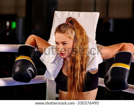 Girl wearing black gloves sitting in corner of boxing ring.