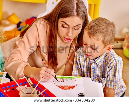 Woman with kids holding colored paper and glue on table in kindergarten .