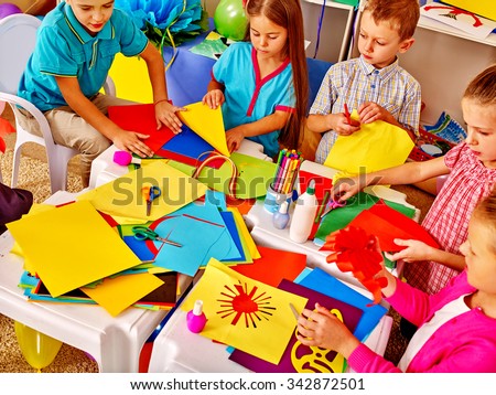 Large Group kids holding colored paper on table in kindergarten .