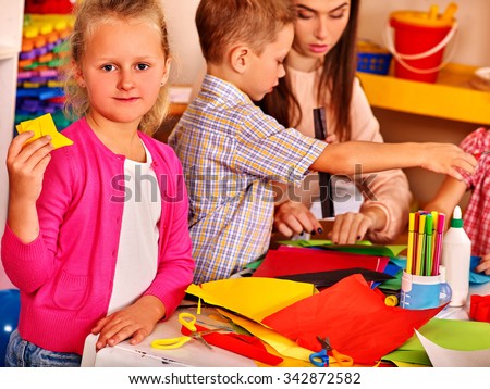 Group kids holding colored paper on table in kindergarten . Look at camera.
