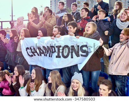 Sport fans holding very big champions banner  and singing on tribunes. Group people.