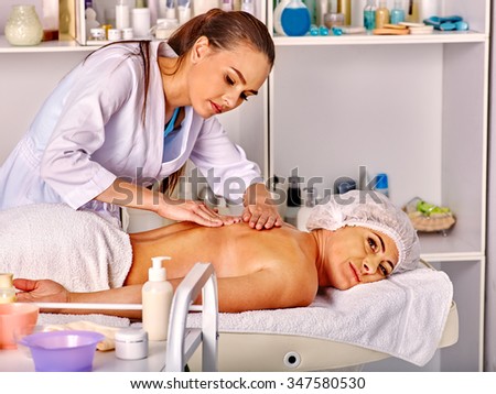 Woman middle-aged take back massage in spa salon with young beautician. Table with cosmetics in foreground.