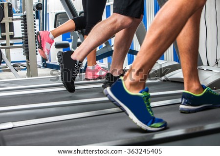 Group of legs wearing sneakers running on treadmill.