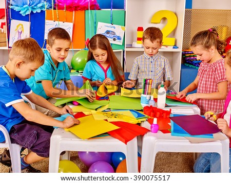 Group kids holding colored paper on table in kindergarten. Kids learning do origami.