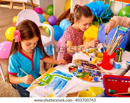 Two girls paint colors. Balloons in the background.