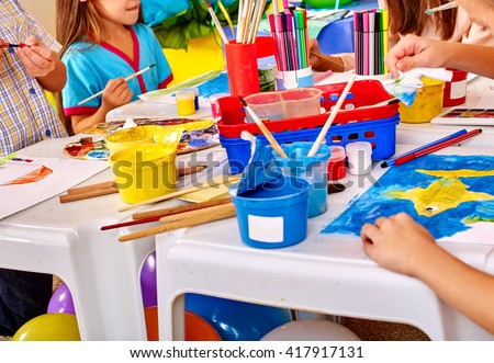Group of children hands  painting on paper at table  in  kindergarten . Paint lesson.