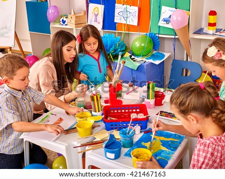 Children with teacher woman painting on paper at table  in  kindergarten . Children learn painting in start school.