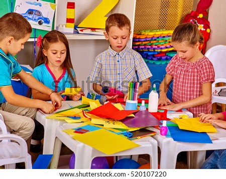 Children with teacher are making something out of colored paper on table in primary school. Children craft lesson in primary school.