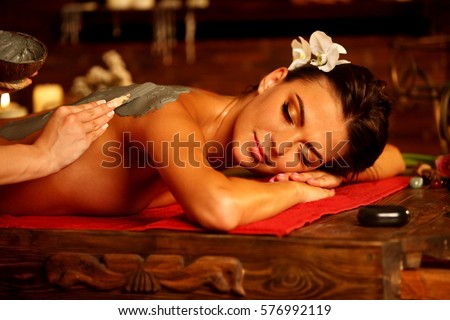 Mud mask of woman in spa salon. Back massage with clay full body . Girl on Luxary interior with candles in oriental therapy room. Female lying on wooden spa bed.