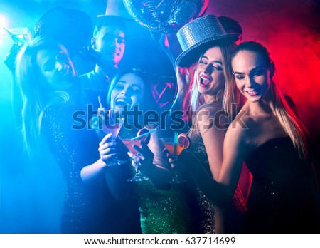 Dance party with group people dancing . Women and men have fun and drinking martini cocktail in night club. Girl on foreground and disco ball color illumination background. Rest after hard day\'s work.