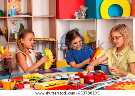 School children with scissors in kids hands cutting paper with teacher in class room. Development and social lerning. Children\'s project in kindergarten. Large group girls and boys together