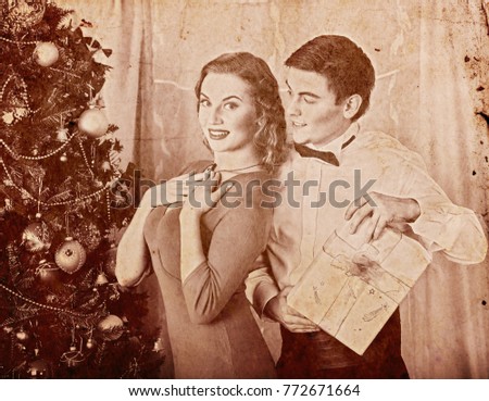 Christmas nostalgy couple on party near Xmas tree take gift box. Happy family on holiday. Vintage sepia old retro photo 1910-1940.