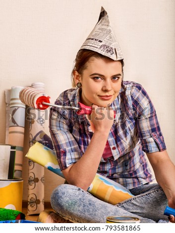 Repair home woman holding paint roller for wallpaper. Painter poses in front of camera. Girl in building newspaper cap renovation apartment .
