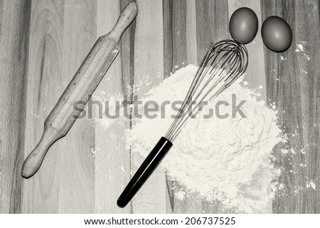 Pastry utensils: eggs, flour, whisk and rolling pin in black and white.