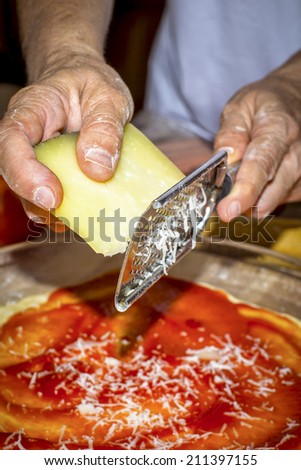 Hands on first plane using a grater, grate cheese for a pizza
