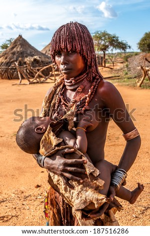 TURMI, ETHIOPIA - MARCH 17,2014 - Hamar woman with child Taye(11m) .Women are adorned with tiny colored beads. Women weave your hair into small braids and paint them red-colored clay.