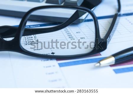 Close up pen and glass with project gantt chart background