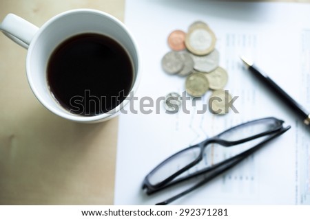 A Cup of coffee with glasses ,coins and pen background