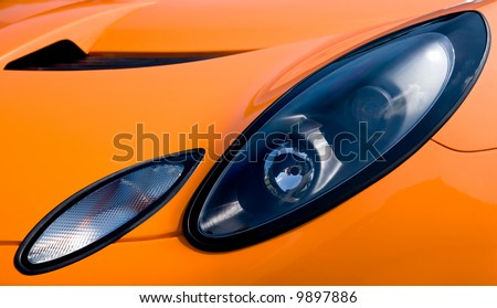 Headlight and hood of a bright orange sports car conveys a feeling of sleekness, power, and speed