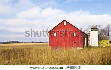 A red barn in a field, with a cloud filled blue sky.
