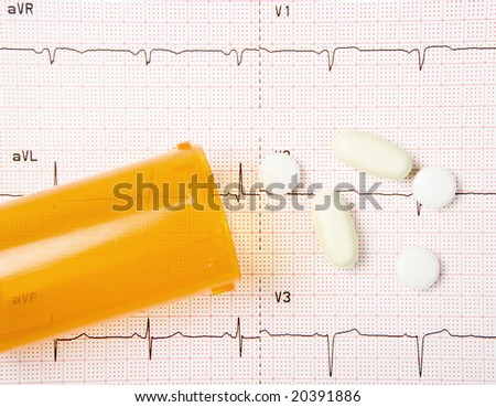 A close up of an electrocardiogram, or EKG, with heart pills and a pill bottle.