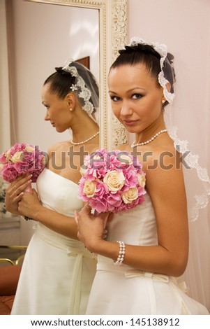 Bride is getting ready for the ceremony in front of the mirror and holding a bouquet.