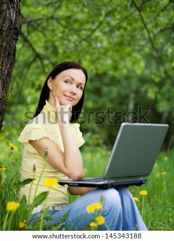 Young woman sitting on the grass with laptop on her knees and thinking about the future or past.