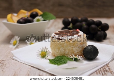 Coconut cake on paper tissue with red wine grapes and mint leaf in front with bowl with banana slices