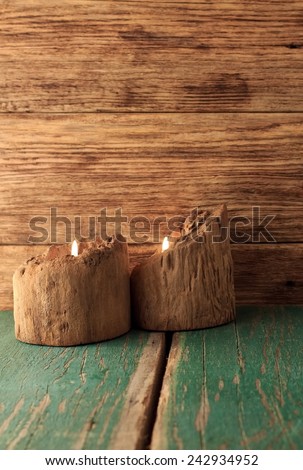 Vertical photo of two candlesticks made from wooden bars placed on wood board with worn green color and with wooden bars in background