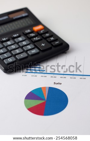 Vertical simple photo with color pie chart printed on paper sheet as main motif and with black calculator in background