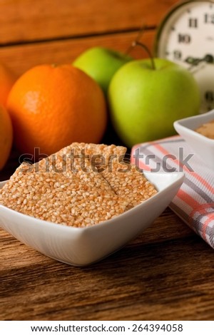 Vertical photo of Biscuits from sesame seeds and honey and fruit in background placed on old worn wooden board with old alarm clock and cloth