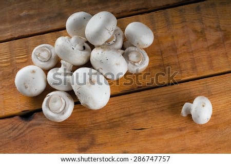 Horizotal photo of pile of small fresh mushrooms champignons on wooden board table with single one out from the heap.