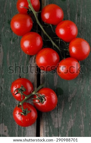 Vertical photo with top view on green worn table and placed two branches of harvested red cherry tomatoes joined by green branch.
