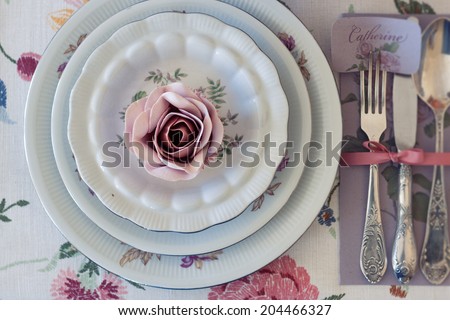 Whimsical place setting with sugar rose cupcake on vintage china. Sweet and romantic detail of tea party table. Perfect for a DIY, vintage or farm wedding. Shallow depth of field.