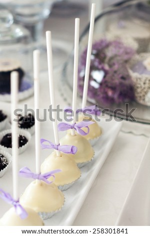 Row of delicious cake pops covered with white chocolate. Close up detail of sweet table at a pastel colored wedding reception.
