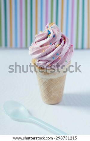 Cupcake in an ice-cream cone - perfect summer dessert for an outdoor birthday party. Strawberry buttercream icing and sprinkles match striped background.