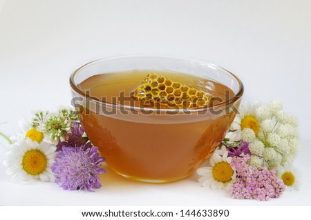 Honey bowl with honeycomb and some wildflowers on white