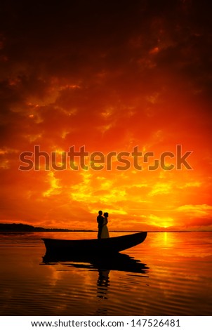 Silhouette of a couple kissing in boat on river in sunset