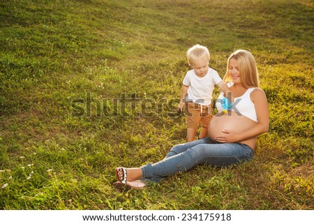 Cute little boy watering his mother\'s pregnant belly in summer nature. Big brother wants his sister to grow faster. Mother\'s day concept.