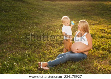 Cute little boy watering his mother\'s pregnant belly in summer nature. Big brother wants his sister to grow faster. Mother\'s day concept