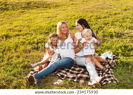 Two young women with kids enjoying sunshine in park. Beautiful pregnant woman with her friend and their kids. Mother\'s day concept.