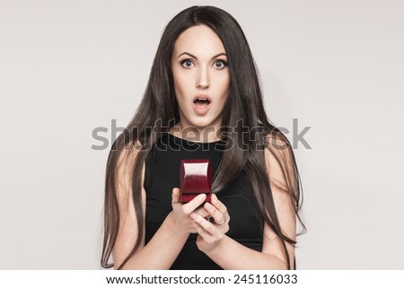 Surprised beautiful woman holding jewelry box with an engagement ring in it. Happy young woman after marriage proposal. White background.