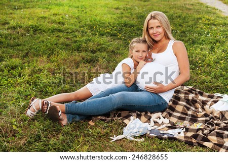 Cute little girl hugging her mother\'s pregnant belly. Happy sister to be is excited about meeting new baby. Mother\'s day concept.