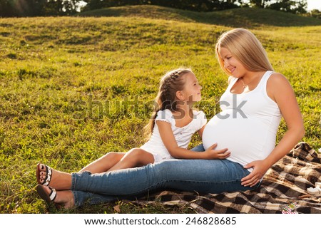 Cute little girl hugging her mother\'s pregnant belly. Happy sister to be is excited about meeting new baby. Mother\'s day concept.