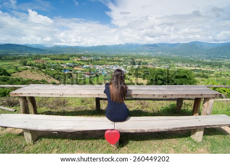 Alone beautiful woman siting on bench on top of mountain and looking at landscape