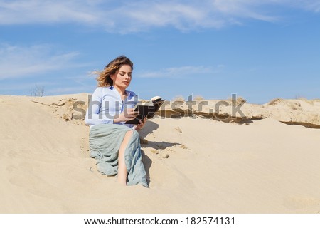 Attractive young blonde woman reading a book on the beach